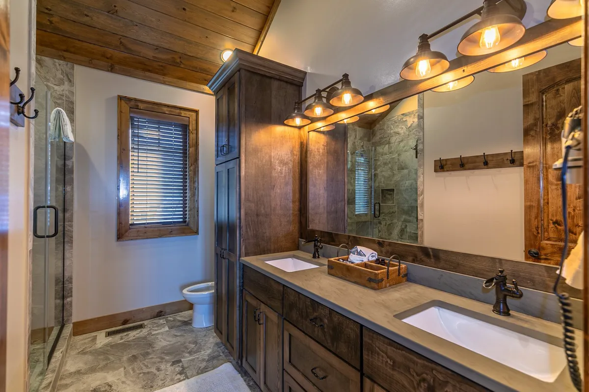 A calm, well-appointed bathroom featuring a double sink vanity, expansive mirror, wooden cabinetry, and a spacious shower area. The space exudes tranquility and is ideal for relaxation and self-care.