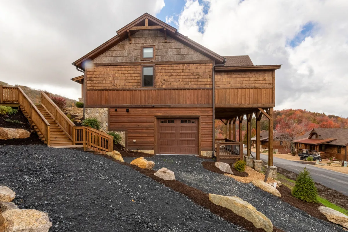 A welcoming view of the home's exterior featuring warm wooden siding, stone accents, a spacious porch, and manicured landscaping. The scene evokes comfort and hints at the inviting communal spaces and outdoor activities available.