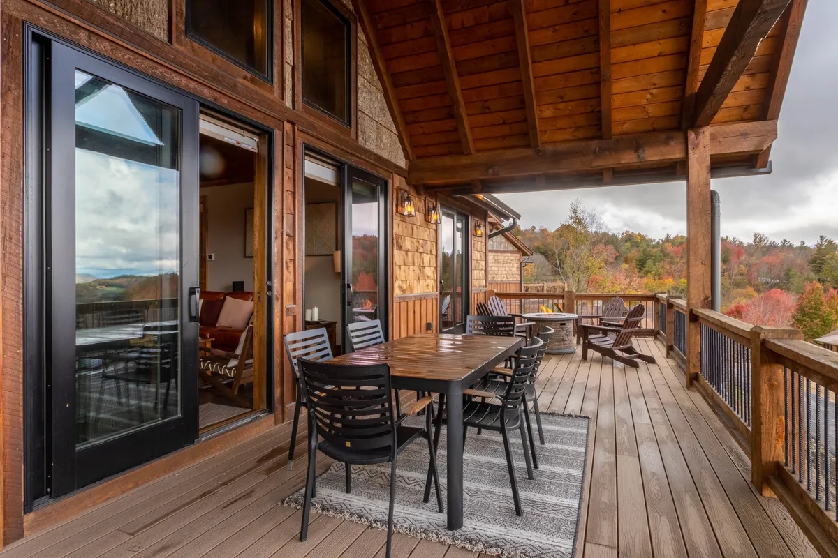 An inviting outdoor dining table sits beneath wooden beams, offering comfortable seating with panoramic views of the landscape. The ambiance is cozy and relaxed, ideal for both morning coffee and stargazing nights.