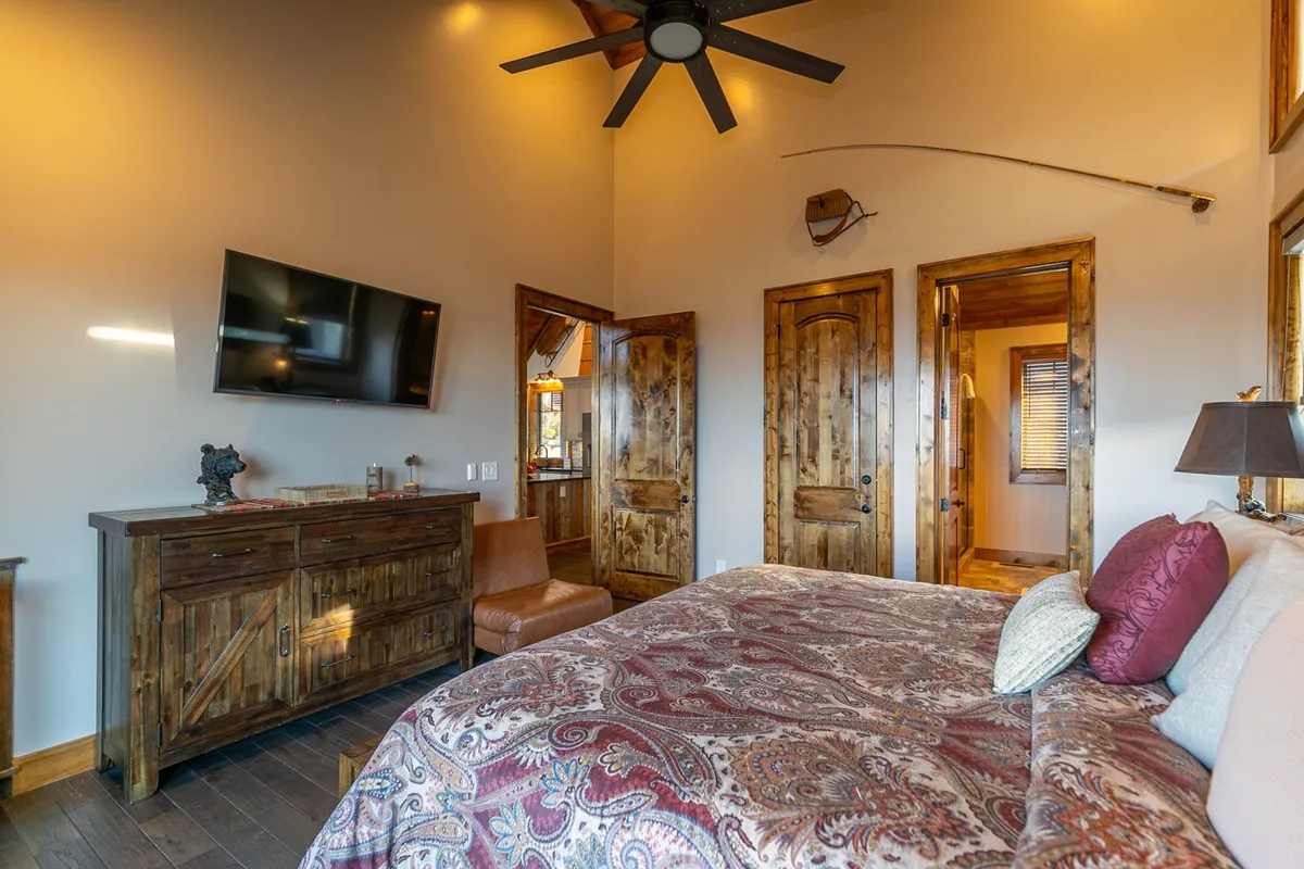 A serene bedroom with a bed dressed in intricate patterned bedding, wooden furniture, and a wall-mounted television. The warm lighting and decor create a relaxing and private sanctuary.