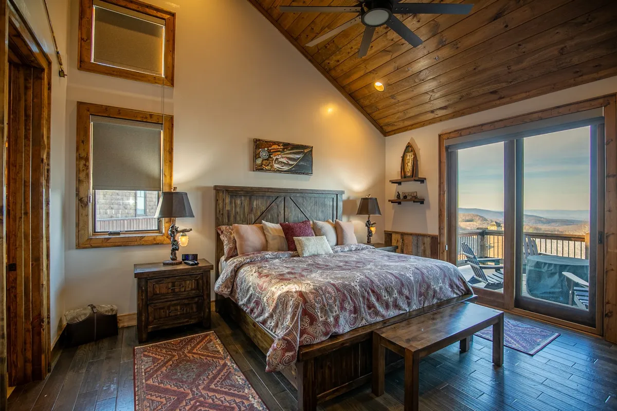 A tranquil bedroom featuring a king-sized bed with decorative bedding, wooden furniture, and large windows that flood the space with natural light and offer scenic views. Soft lighting and tastefully chosen lamps add to the calming ambiance.